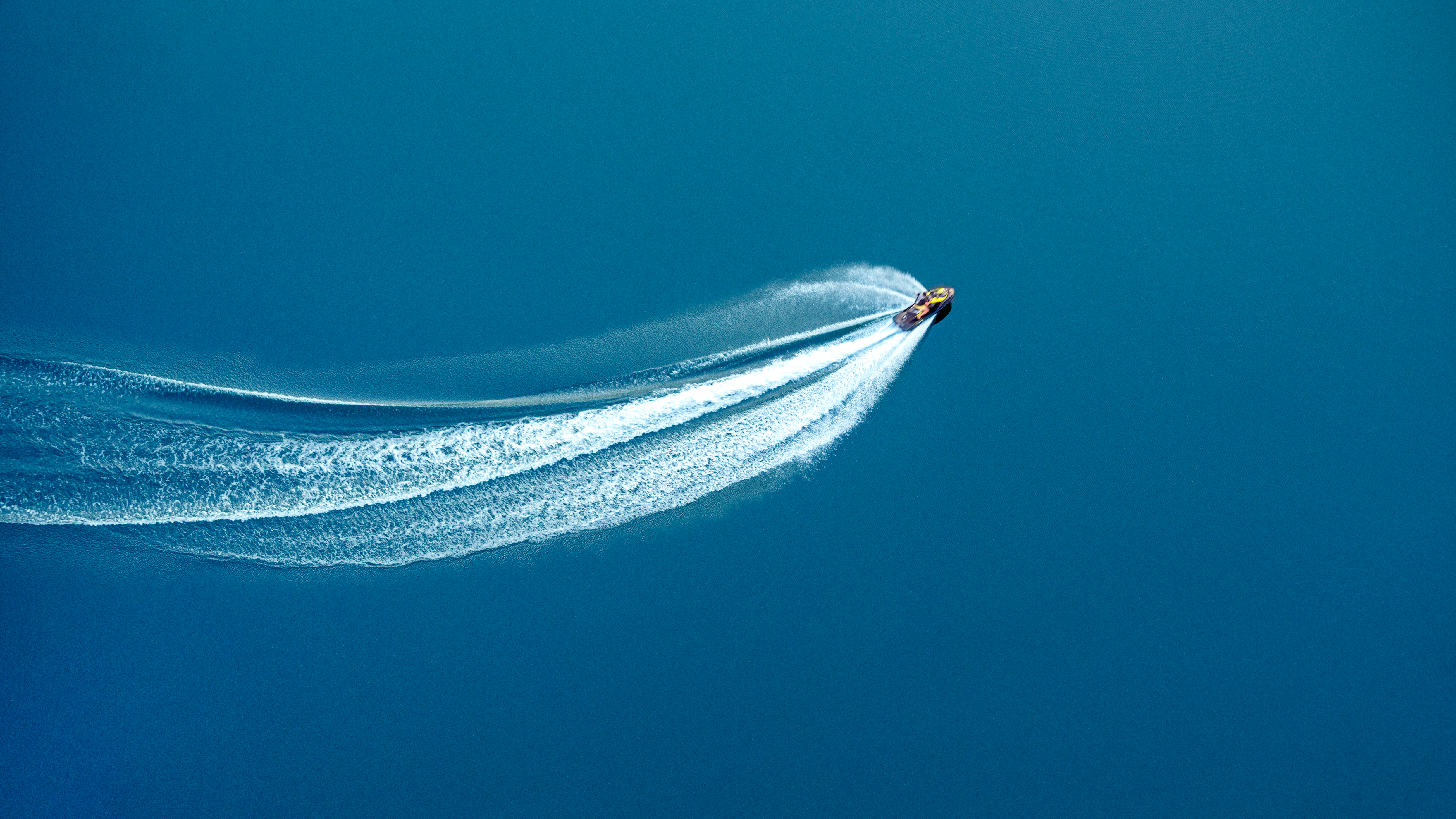 A deep blue ocean with a jetboat cutting a wake through it at high speeds