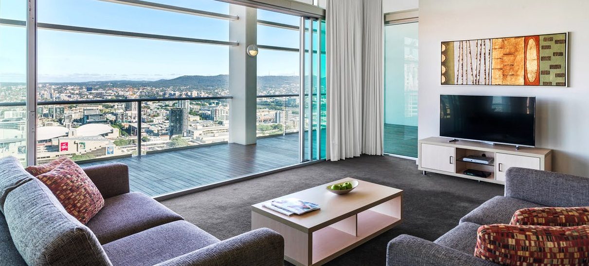 Apartment lounge with sofas and a TV opening onto a balcony with high city views