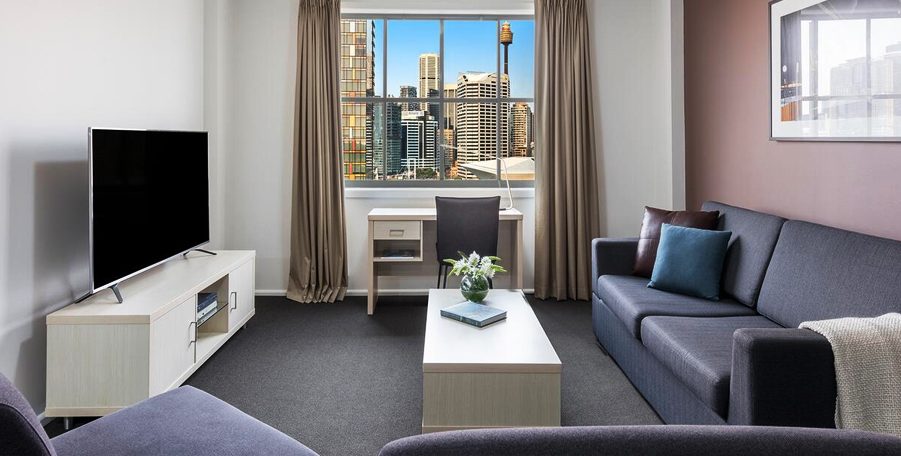 Apartment lounge with a sofa, TV and desk under a window looking onto city towers