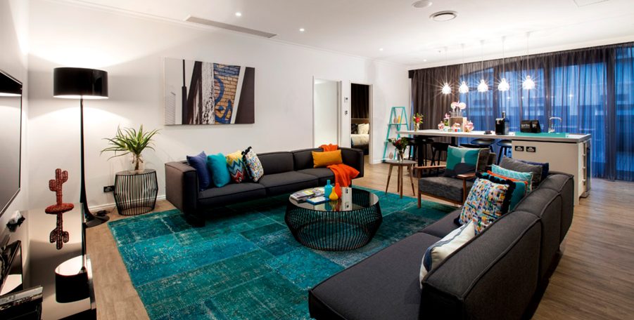 Apartment living room with dark sofas, a teal rug and a kitchen bench