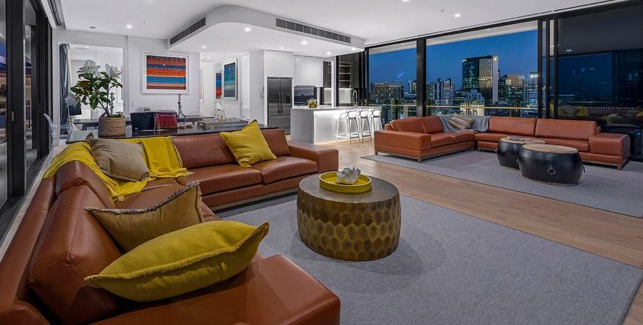 Penthouse living room with tan leather sofas, a kitchen bar and floor-to-ceiling windows onto the city