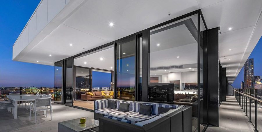 Penthouse terrace with outdoor lounge and dining furniture outside a glass-walled living area at dusk