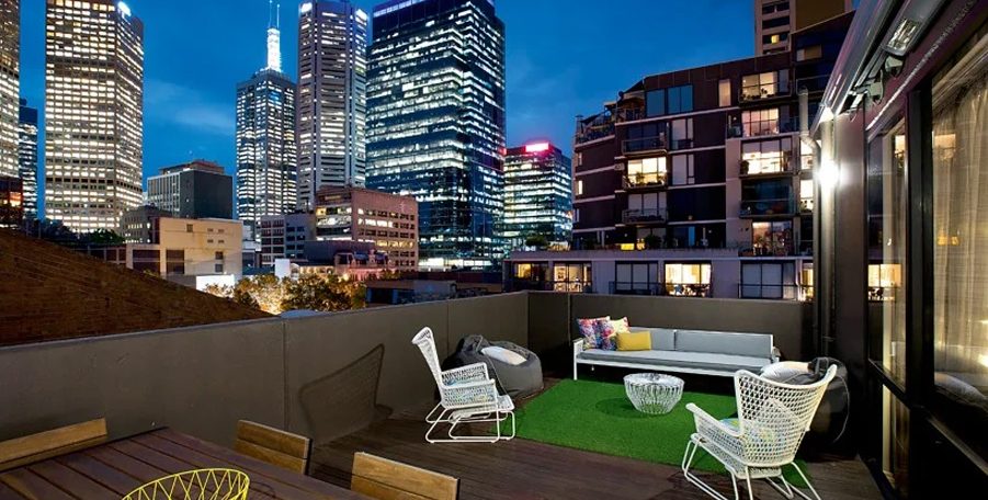 Rooftop terrace with lounge chairs, beanbags and artificial grass beneath lit city towers at night