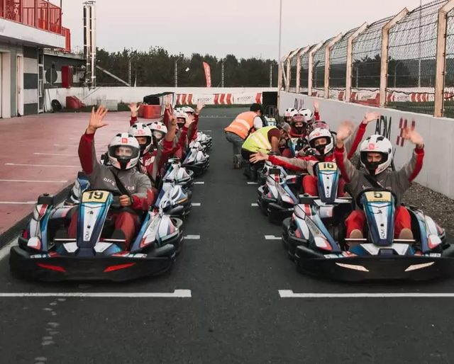 A grid of go-karts lined up with drivers waving