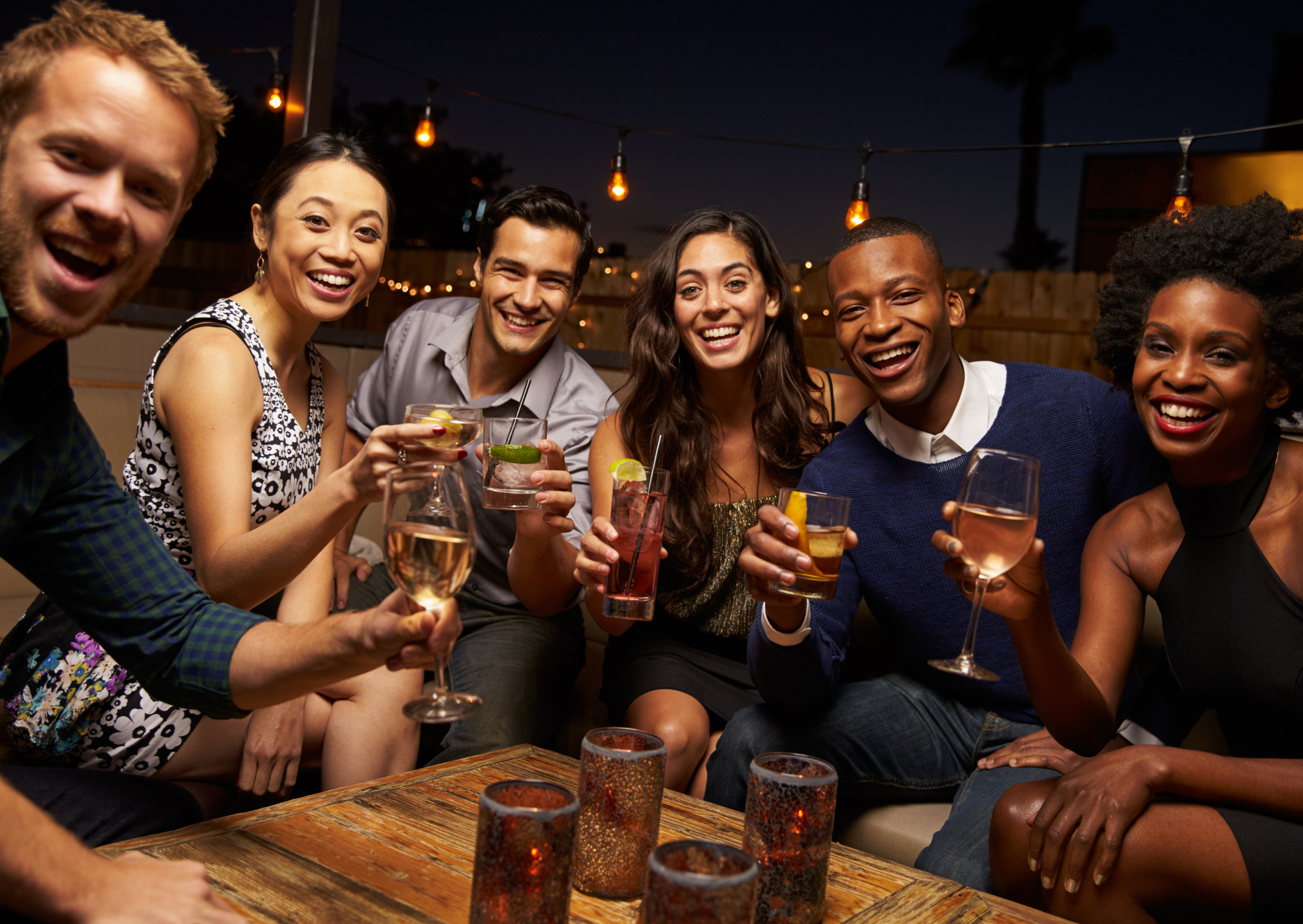 A group of young people around a bougie bar all holding an assortment of drinks and cheersing