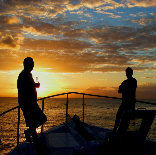 Two blokes on the rail of a boat with a beer, the sun going down over the water