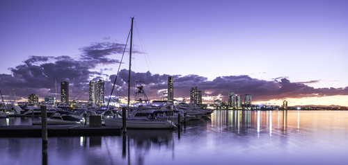 A marina full of yachts with high rise towers behind at dusk