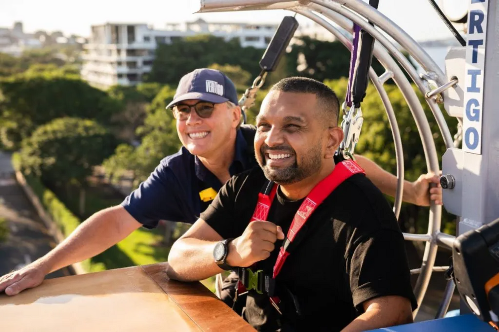 Two blokes harnessed in on a high platform above the trees, grinning before the drop