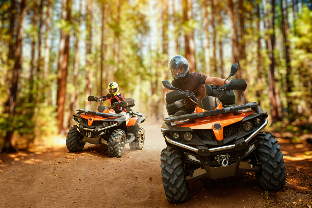 Two blokes on quad bikes on a dirt track through the trees