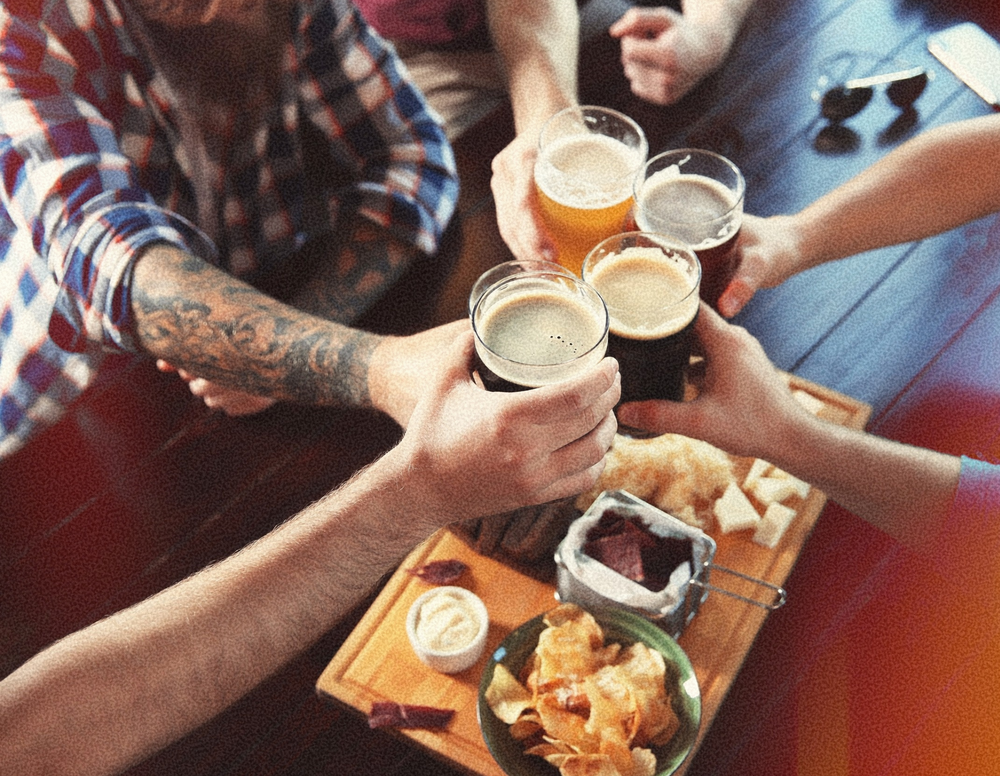 Mates clinking beers over a table of bar snacks