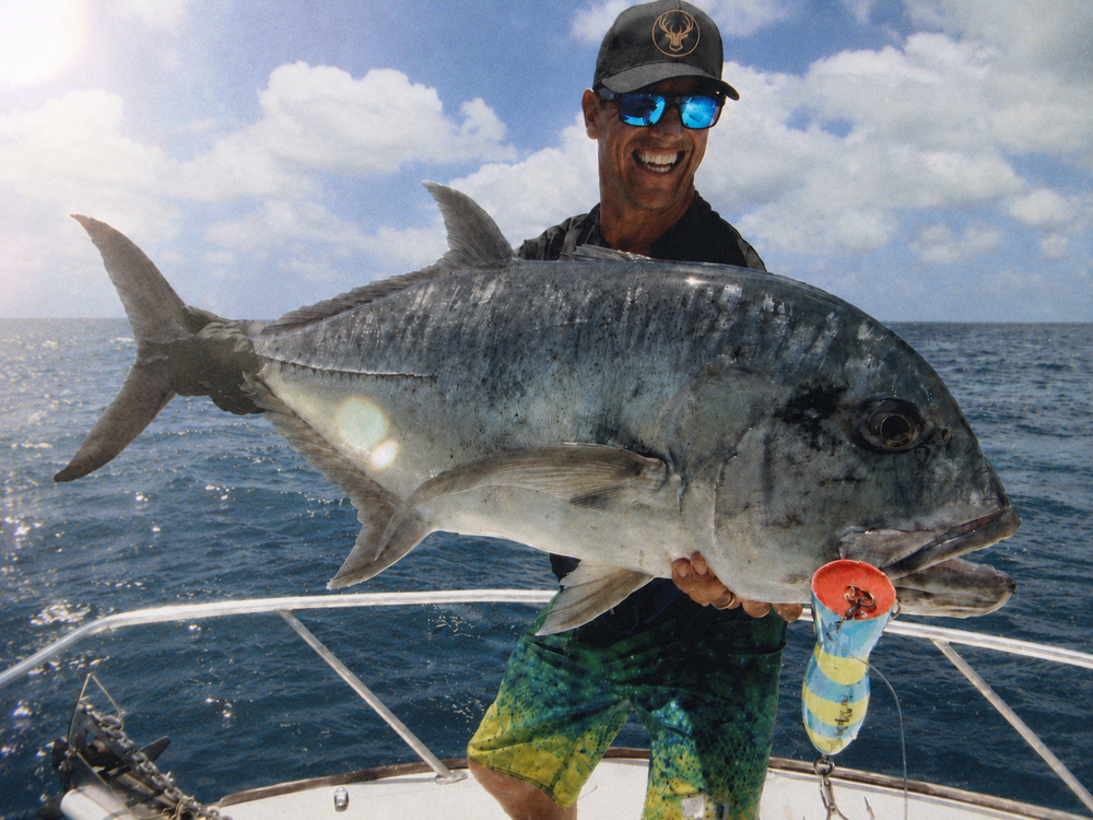 A bloke in sunglasses holding up a big fish on the back of a boat