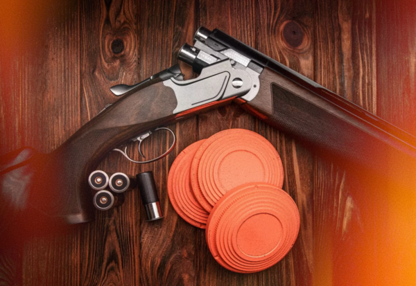 A shotgun lying beside orange clay targets on a timber table