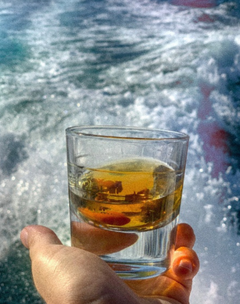 A glass of spirits held out over the wake of a boat