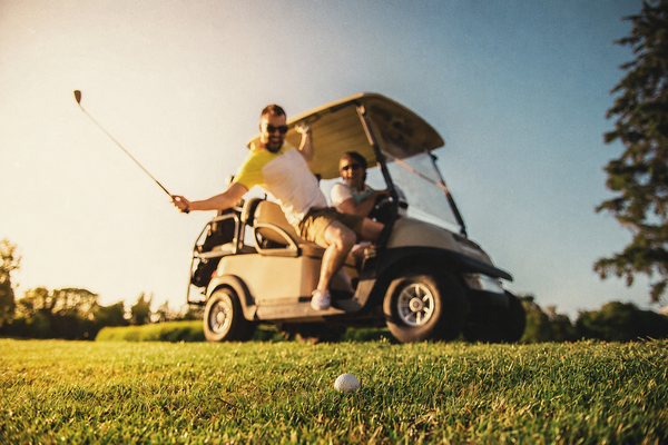 A golfer mid-swing beside a golf cart on the fairway