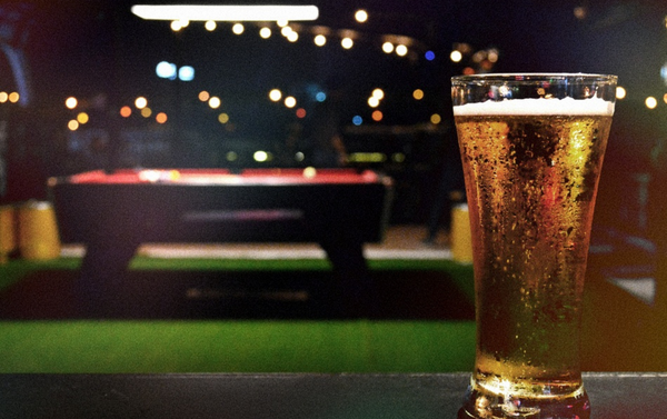 A pint of beer in front of a pool table in a dim bar