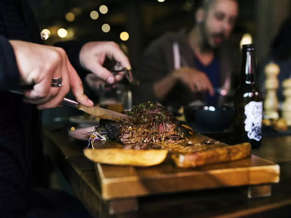 A steak being sliced on a wooden board at the dinner table