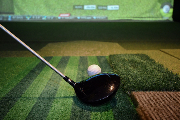 A driver lined up behind a teed-up ball in front of a golf simulator