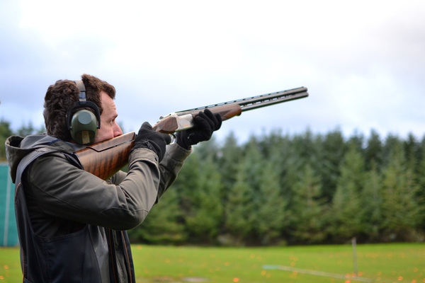 A shooter in ear protection aiming a shotgun on a clay range