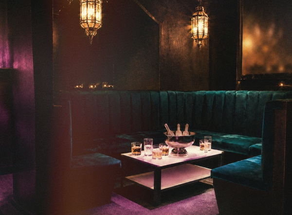 A private booth in a dark lounge bar, drinks waiting on the table