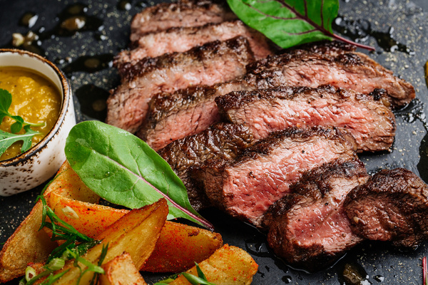 Sliced steak served with greens and a dipping sauce