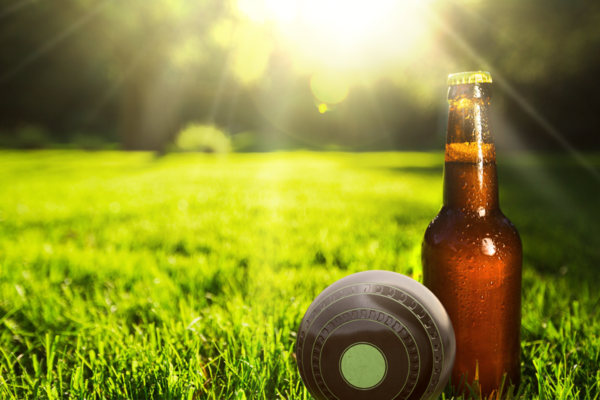 A beer bottle on the green beside a lawn bowl