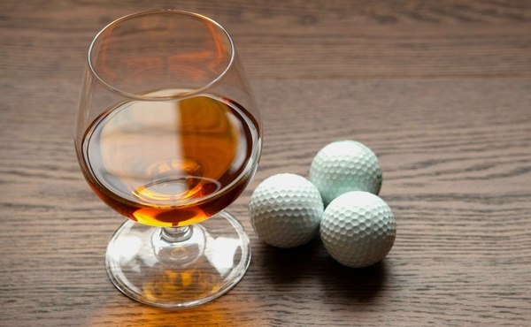 A glass of whisky beside three golf balls
