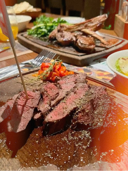 Sliced steak on a board with a feast spread out behind it