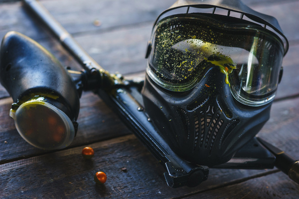 A paintball mask lying beside a marker and spent paintballs