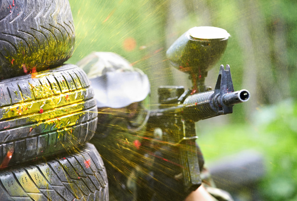 A paintball marker aimed from behind a stack of tyres