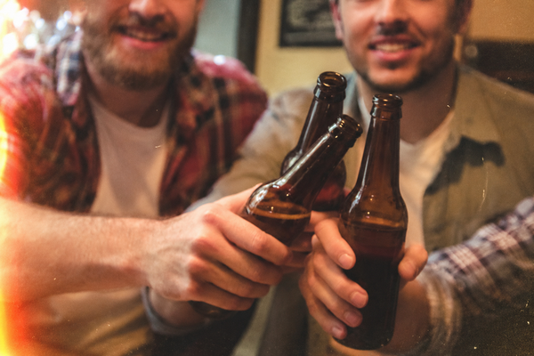 Two mates grinning as they clink beer bottles