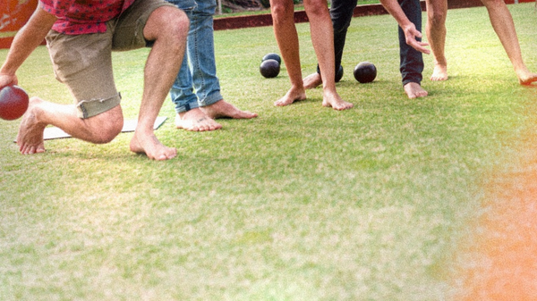 A barefoot bowler sending one down while his mates watch