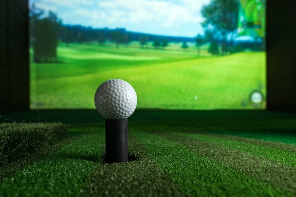 A golf ball on a tee in front of a simulator screen