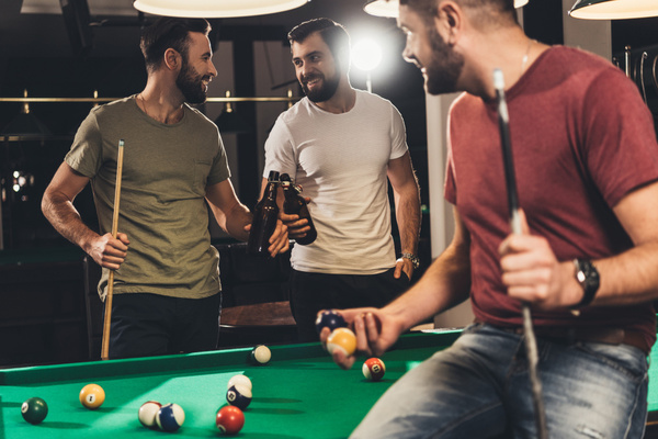Mates playing pool with beers in hand