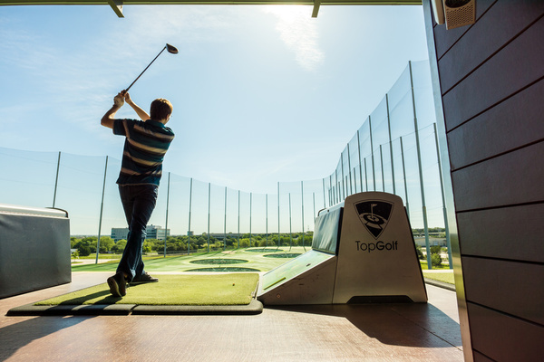 A golfer swinging in a driving range bay