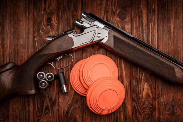 A shotgun and orange clays on a timber table
