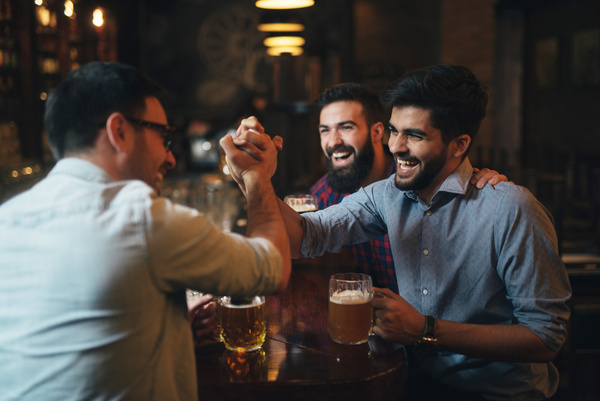 Three mates toasting with beers at a bar