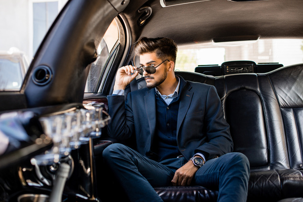 A bloke in a suit lounging in the back of a limo