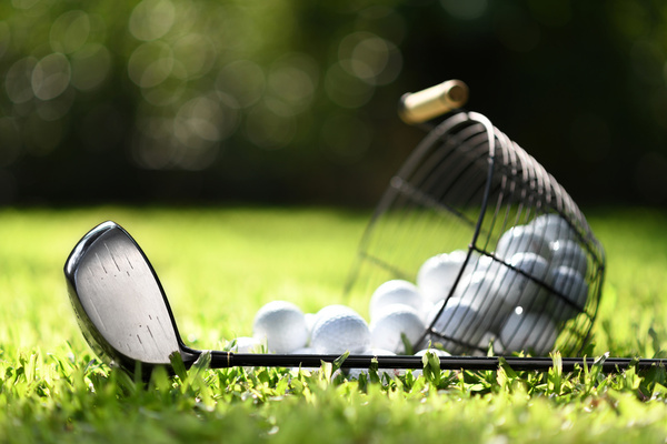 A golf club and a basket of balls on the grass