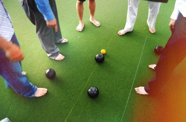 Barefoot blokes standing around the bowls on a green