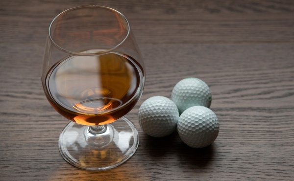 A glass of whisky beside three golf balls