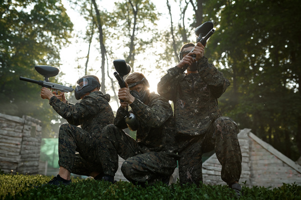 A paintball squad crouching behind a wall in the trees