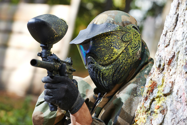 A paintballer in a camo mask aiming his marker