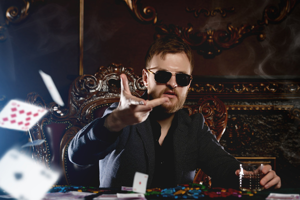 A bloke in sunglasses flicking cards at a poker table