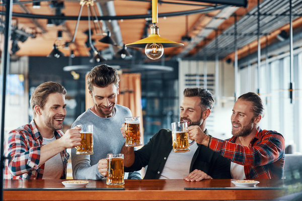 Four blokes toasting with beers at a long bar table